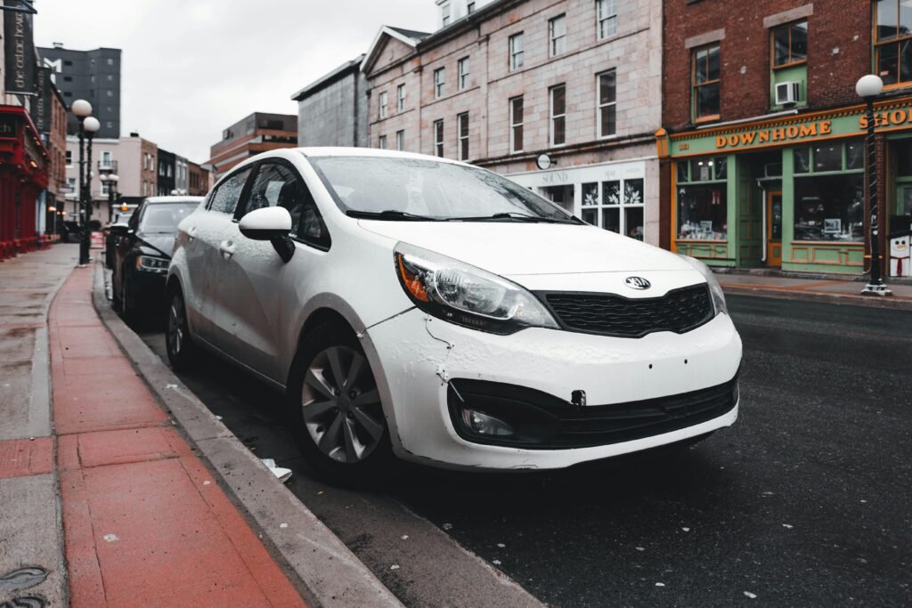 White Kia parked on a wet street with urban buildings in the background after rain.