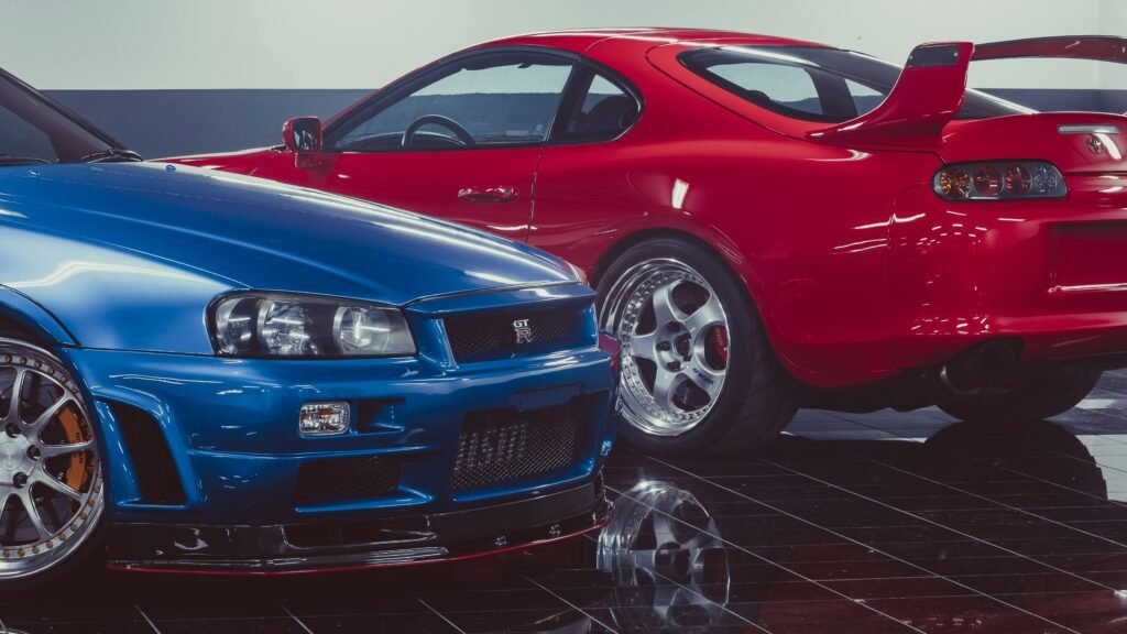 Blue Nissan Skyline GT-R and red Toyota Supra parked in a showroom.