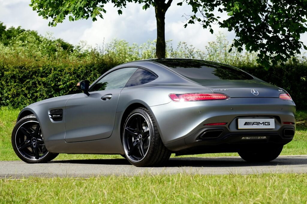 A luxury Mercedes AMG GT in silver, parked outdoors by trees on a sunny day.