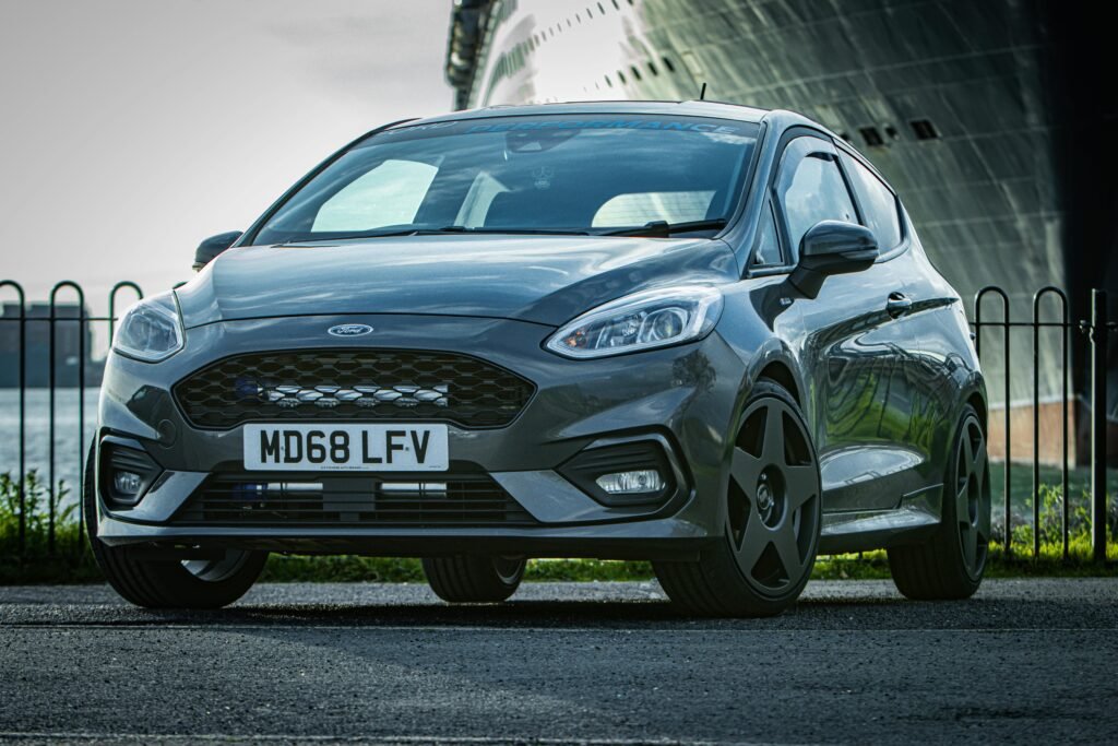 Gray Ford Fiesta ST parked on urban street with nautical backdrop, stylish and sleek design.