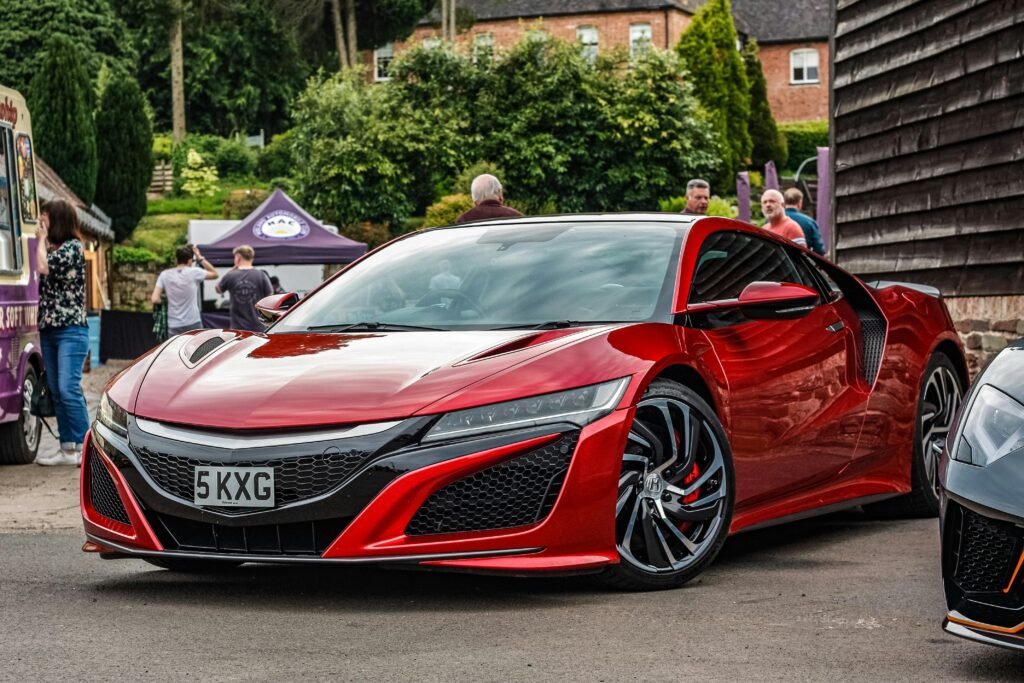 A sleek red sports car, Honda NSX, parked at an urban event with people in the background.