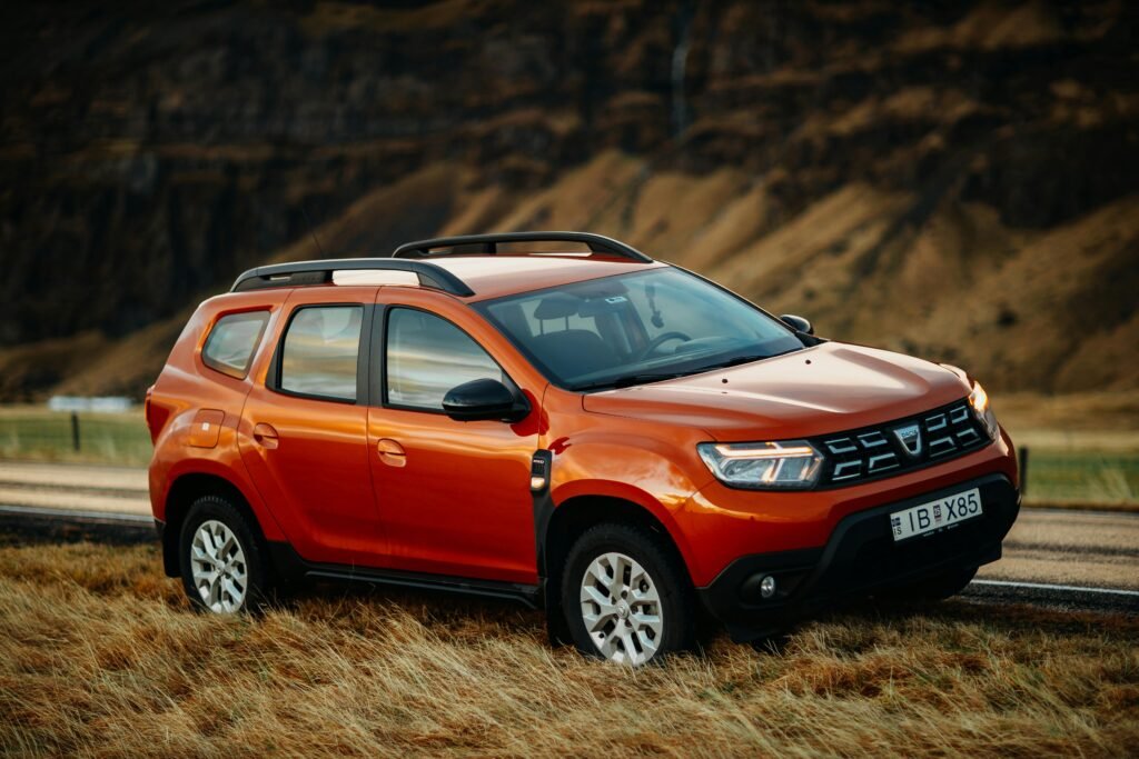 A second-generation red Dacia Duster SUV parked on a rural roadside, showcasing its subcompact crossover design.