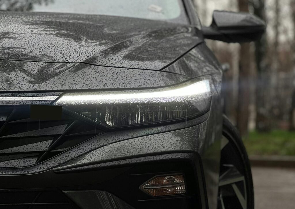 Detailed shot of a car headlight with rain droplets, highlighting modern automotive design.