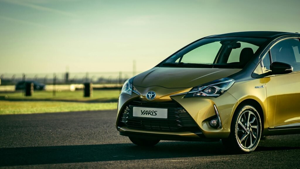 Sleek yellow Toyota Yaris parked on a sunlit asphalt road outdoors.