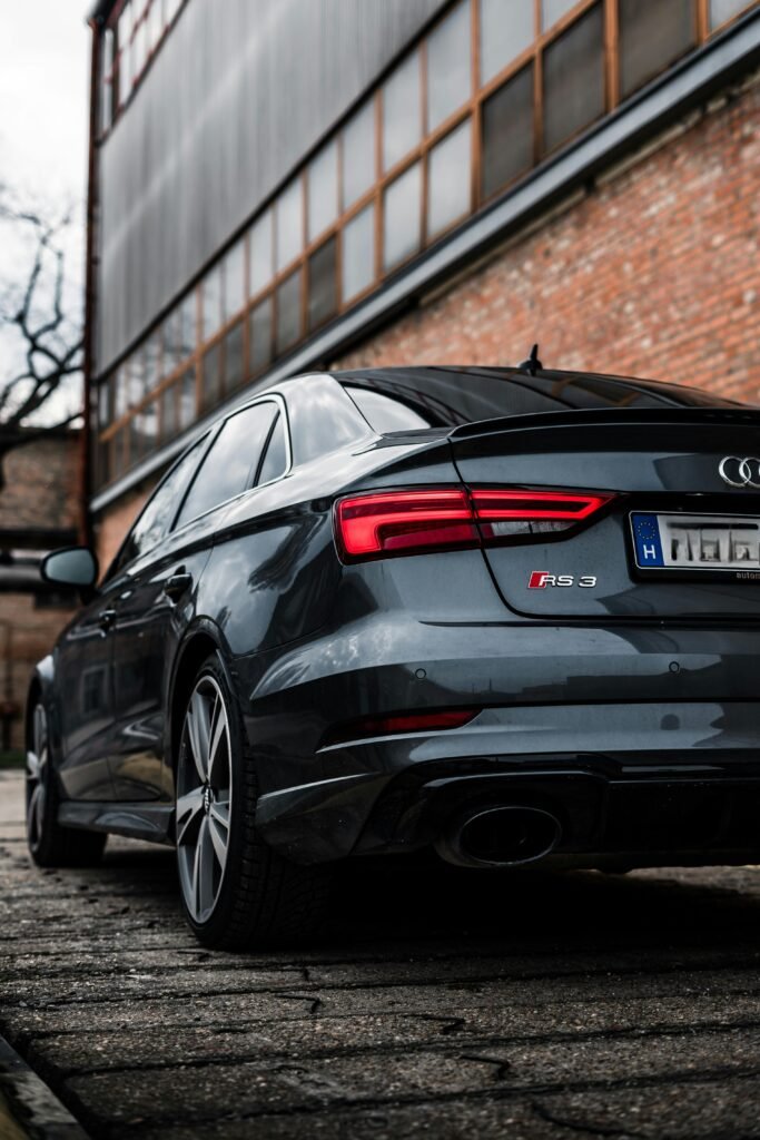 Black Audi RS 3 parked outdoors near a brick building, emphasizing luxury and performance.